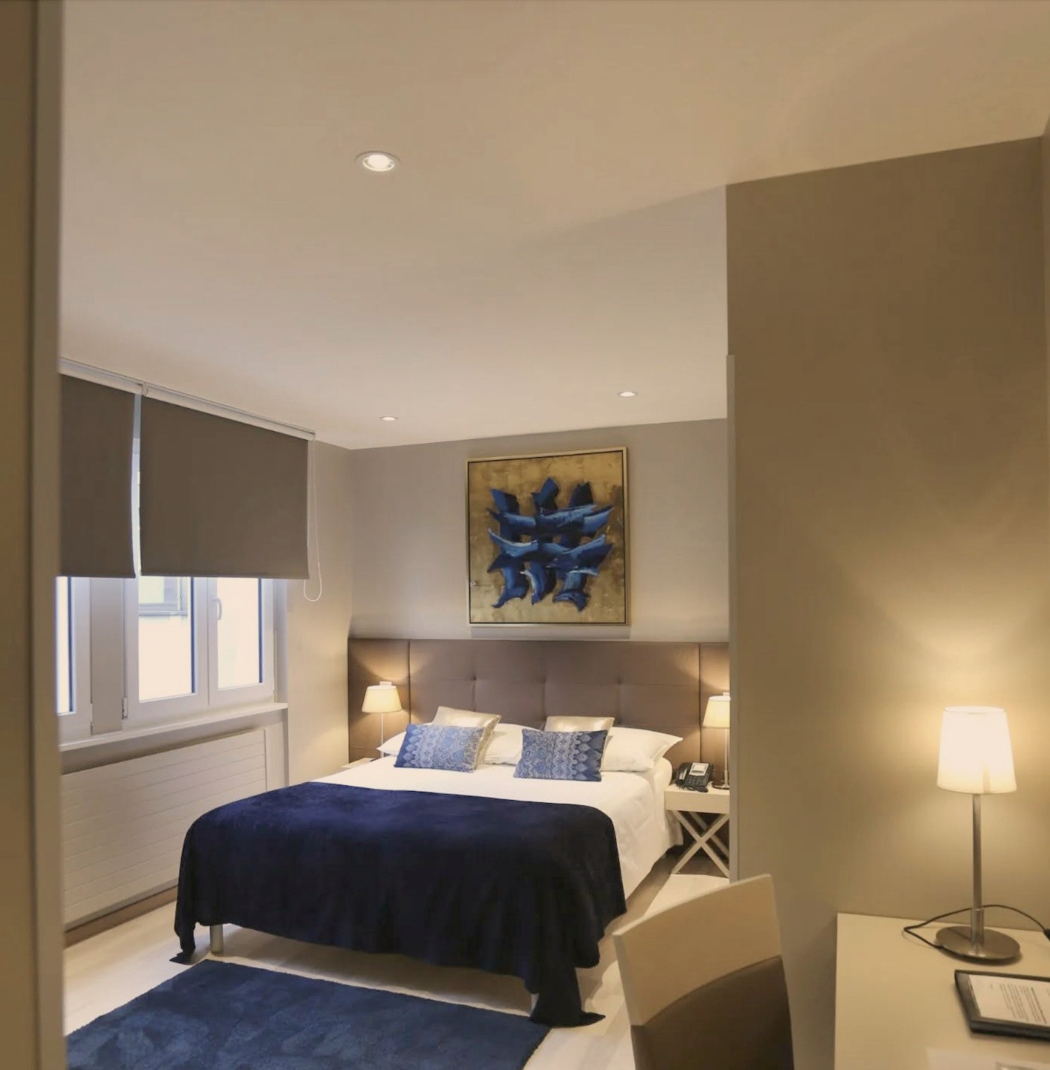 Chambre rénovée de l’Hôtel Excelsior à Genève, lit double à tête de lit rembourrée et linge bleu nuit