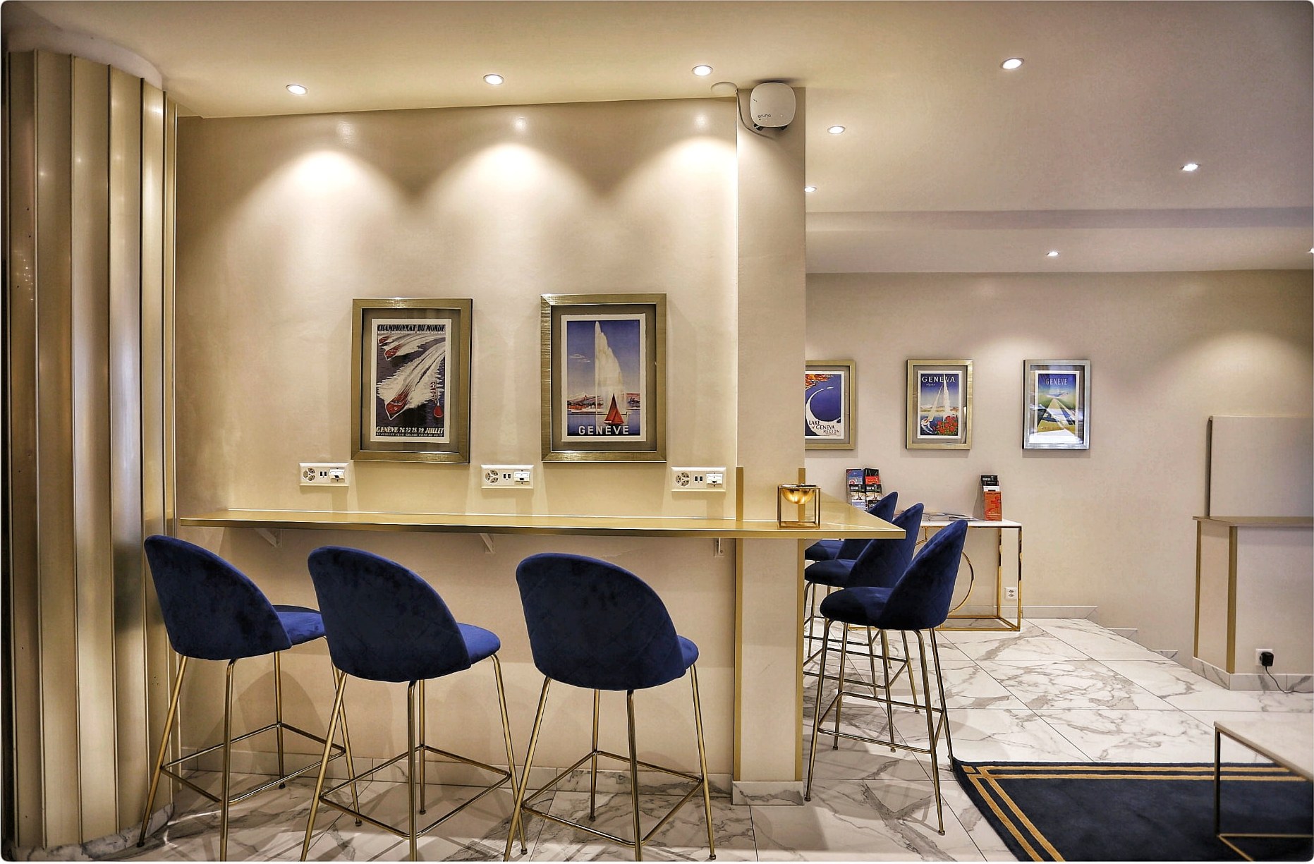 Comptoir doré et tabourets bleu nuit du salon de l’Hôtel Excelsior à Genève, affiches anciennes de Genève au mur